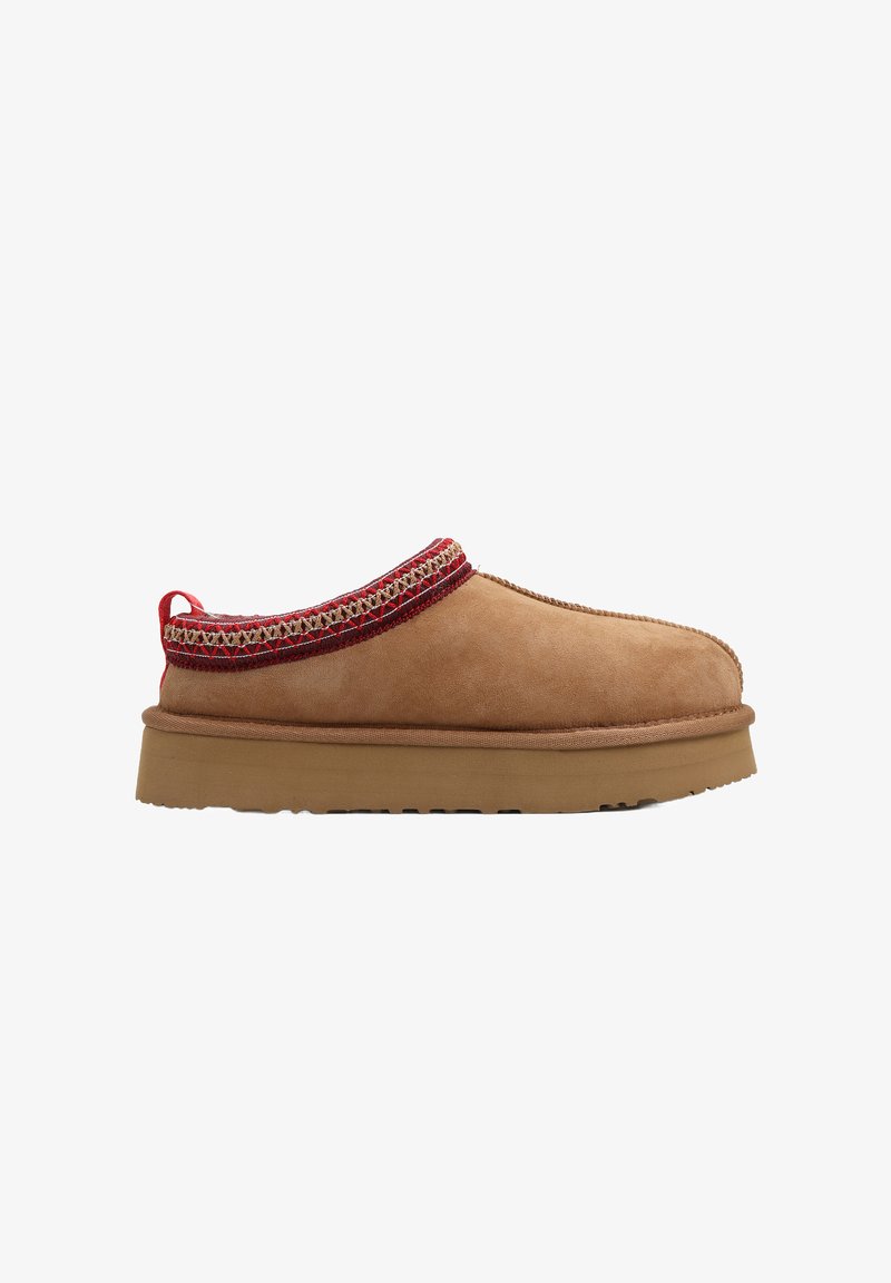 Brązowy zamszowy wsuwany but z zaokrąglonym noskiem, czerwoną ozdobną nitką wokół kołnierza oraz teksturowaną gumową podeszwą.