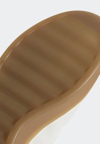 GummiskosULA med en brun färg, texturerad yta med horisontella spår och en slät kant som övergår till ett vitt övermaterial.