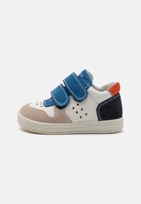 Basket multicolore avec des bandes Velcro bleues, un mélange de matériaux blancs, beige et marine, avec des détails perforés sur le bout.