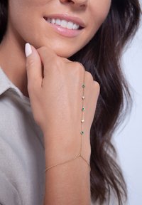 Pulsera de cadena de oro que presenta gemas verdes alternas y cristales transparentes, con un diseño delicado que se ajusta con elegancia sobre la muñeca.