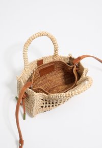Woven straw handbag with tan leather handles. Open top design showcases a textured brown interior and leather tag label.