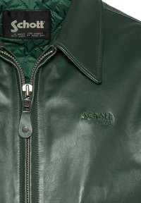 Groene leren jas met een ritssluiting, platte kraag, gewatteerde binnenvoering en reliëf Schott-logo op de borst. Glad textuur.