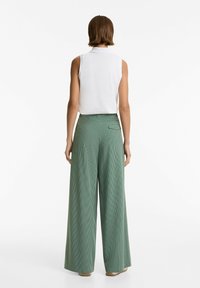 Top sans manches blanc et pantalons larges verts taille haute avec un motif à carreaux et un détail de poche arrière. Tissu lisse avec une coupe décontractée.