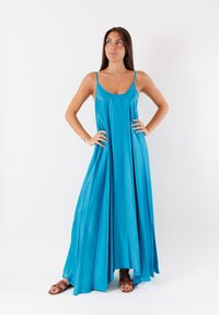 Un lungo vestito fluente in tessuto blu brillante, con sottili spalline a spaghetti e una silhouette rilassata, che si adagia elegantemente fino a terra.