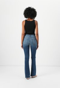Black ribbed tank top paired with flared blue denim jeans featuring a mid-rise waist and back pockets, displayed from a rear view.