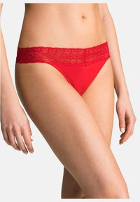 Slip rossi con una cintura in pizzo, caratterizzati da un corpo liscio e delicati dettagli in pizzo lungo il bordo superiore.