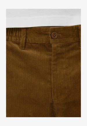 Pantalon en velours côtelé marron avec texture à côtes verticales, doté d'une fermeture à boutons et de passants pour ceinture. Le matériau semble doux et résistant.
