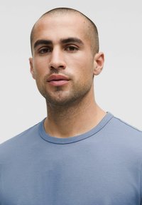 Tricou albastru deschis cu guler rotund, mâneci scurte, textură netedă, design mulat, cusături minime, prim-plan al gulerului și toracelui superior.