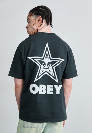 Black cotton t-shirt featuring a large white star graphic with a face, and the word "OBEY" in bold white letters on the back.