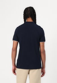 Navy blue polo shirt featuring a classic collar, short sleeves, and contrast trim at the cuffs. Made from smooth, soft fabric.