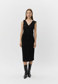 Must kleit pitsist V-kaelusega, kroolitud ümber keha ja põlveni ulatuva seelikuga. Sobitatud kõrgete, läikivate mustade krokodillimustriliste saabastega.