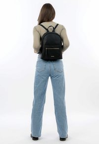 Zaino in pelle nera con superficie texture, forma arrotondata, spallacci regolabili e tasca anteriore con zip.
