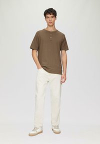 Braunes kurzärmliges Henley-Shirt mit einem Dreiknopfverschluss, kombiniert mit hellbeigen geraden Hosen und hellen Sneakers.