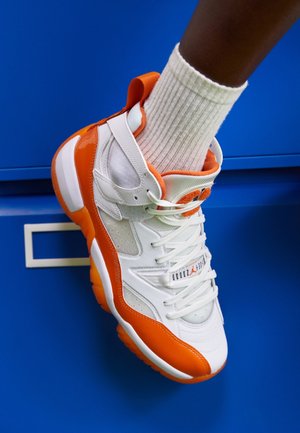 Biało-pomarańczowy wysoki sneaker z sznurowadłami noszony na stopie, na niebieskim tle, zestawiony z białymi prążkowanymi skarpetkami.