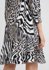 Svartvitt klänning med ett abstrakt djurtryck, med beige detaljer och en utsvängd nederkant. Tillverkad av lätt, slät tyg.