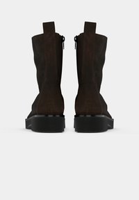 Bottines en suede marron avec une semelle noire plate, dotées de fermetures éclair de chaque côté et de petites languettes en haut pour un enfilage facile.