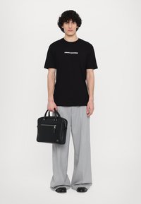Svart bomull t-skjorte med "Armani Exchange"-logo, grå skreddersydde bukser og en strukturert svart skinnkoffert med glidelås og håndtak.
