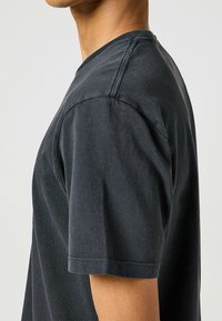 Camiseta de algodón gris oscuro con cuello redondo, mangas cortas y detalles de costura visibles. Textura suave y corte relajado.