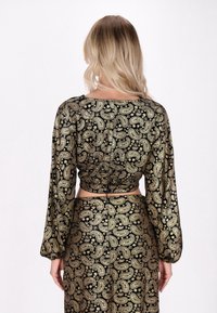 Svart crop top med lång ärm, prydd med ett guld paisleymönster. Tyget har en mjuk textur och samlingsdetalj i ryggen.