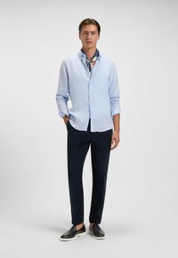 Jasnoniebieska, długorękawowa koszula z guzikami i podwiniętymi mankietami, zestawiona z granatowymi spodniami i ciemnymi butami wsuwanymi, z wzorzystą chustą.