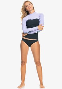 Traje de neopreno de manga larga en lavanda y negro, con acentos florales en las mangas. El material parece elástico y ajustado, ideal para deportes acuáticos.
