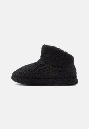 Black slipper with a textured, fuzzy exterior. Ankle-high design with a rounded toe and soft, flexible sole for comfort.