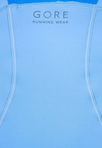 Ljusblå löptröja med platta sömmar och GORE-logotyp. Tillverkad av ett slätt material, med rundad hals och förstärkta områden för hållbarhet.