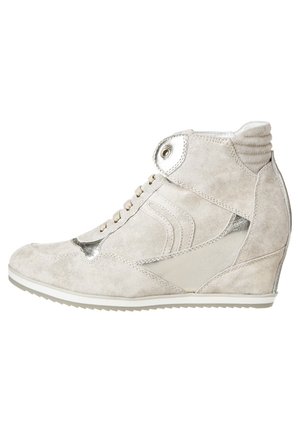 Beżowe zamszowe sneakersy w stylu high-top z metalowymi akcentami, z obcasem w kształcie klinu, okrągłym noskiem i tonującym przeszyciem. Zawiązywane z przodu z ozdobnymi elementami.