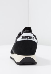 Baskets de course noires en daim et en maille avec un accent de talon blanc et "SAUCONY" imprimé en noir. Comprend une semelle intermédiaire blanche et une semelle extérieure texturée noire.