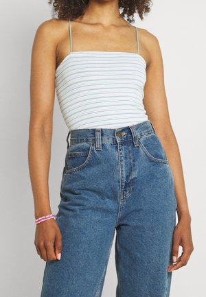 Gestreept tanktop in lichtblauw en wit, gecombineerd met high-waisted spijkerbroek. Opvallende details zijn dunne schouderbandjes en een armband.