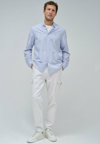 Camisa de botones a rayas azul y blanca combinada con pantalones cargo blancos y zapatillas blancas. Tejido suave, corte relajado y un aspecto moderno.