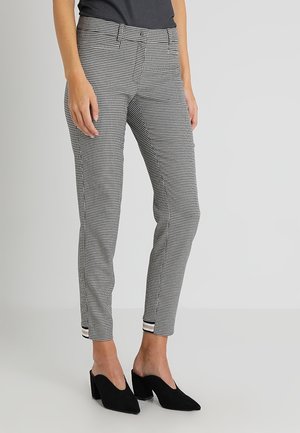 Pantalons à motif pied-de-poule noir et blanc avec une coupe slim, présentant un devant plat, des poches latérales et un ourlet retroussé. Associés à des talons noirs.