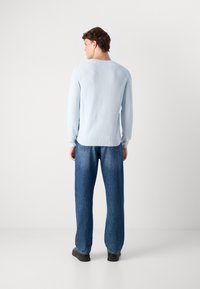 Light blue knitted sweater with long sleeves, crew neck, and ribbed hem, paired with loose-fitting dark denim jeans and black shoes.