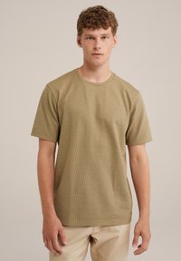 Camiseta de manga corta color verde oliva con escote redondo, tela texturizada y corte relajado. Combinada con pantalones beige claros.