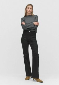 Harmaa neulepaita pitkillä hihoilla, yhdistettynä korkeavyötäröisiin mustiin levenneisiin farkkuihin. Ruskeat mokkasiinit, joissa on terävät varpaat.