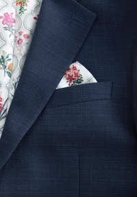 Veste de costume texturée bleu marine avec une doublure florale et un mouchoir de poche blanc orné de fleurs rouges et vertes.