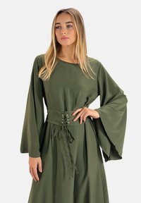 Robe vert olive avec de longues manches en cloche, un corsage ajusté et un détail de taille à lacets. Matériau doux et drapée élégante.