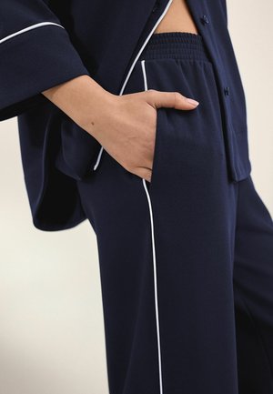 Set de lounge bleumarin, cu bluza cu nasturi și pantaloni cu talie elastică și detalii albe pe margini. Țesătură moale, cu croială lejeră.