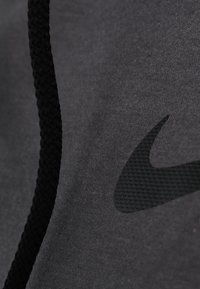 Tissu gris à texture lisse avec un logo Nike noir. Un cordon tressé noir est visible, ajoutant un détail fonctionnel.