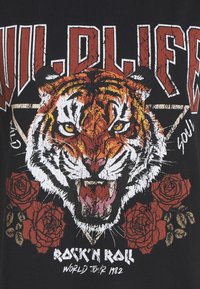 Tête de tigre avec la bouche ouverte, entourée de roses rouges et de texte stylisé indiquant "Wild Life" et "Rock'n Roll World Tour 1982" sur fond noir.