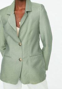 Vaaleanvihreä bleiseri, joka on valmistettu teksturoituneesta kankaasta ja jossa on nuottikaulus, kaksi kultasävyistä nappia ja sivutaskut.