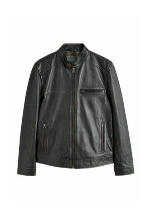 Mężczyzna z krótkimi włosami i brodą, ubrany w czarną skórzaną kurtkę na zamek z zamykaną na zamek kieszenią na piersi na jednolitym tle.