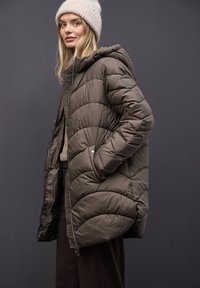 Chaqueta tipo plumas en un color oliva apagado, con un diseño acolchado, capucha, bolsillos laterales y un parche con el logo en la manga izquierda.