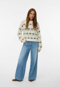 Pull en maille avec des motifs floraux verts et roses, sur un fond crème clair ; associé à un jean bleu à coupe large. Chaussures marron.