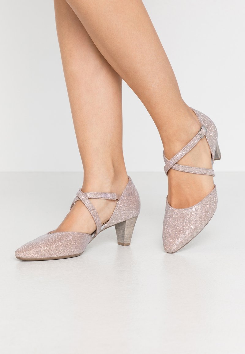 Scarpe da donna rosa scintillanti con cinturini incrociati, punta affusolata e tacco in legno basso, caratterizzate da una finitura glitterata testurizzata.