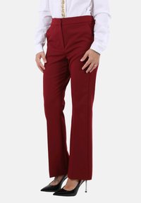 Pantaloni rossi su misura in tessuto liscio, con vita alta, gambe dritte e tasche laterali, abbinati a décolleté nere con punta.