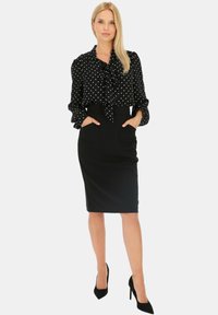 Czarna bluzka w białe kropki, z kokardą i falbaniastymi rękawami, w połączeniu z dopasowaną czarną spódnicą ołówkową z bocznymi kieszeniami.