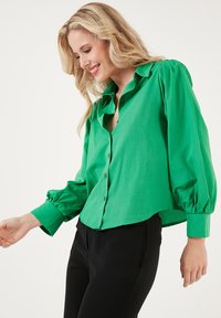 Camicia verde button-up con maniche lunghe a sbuffo, realizzata in tessuto morbido. Presenta una vestibilità rilassata e un orlo arrotondato, abbinata a pantaloni neri.