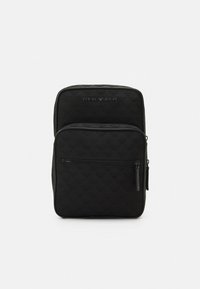 Zaino nero trapuntato con una texture liscia, dotato di una tasca frontale con cerniera, maniglia superiore e logo impresso sul pannello anteriore.