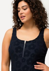 Navyblauwe bloemen tanktop met textuurpatronen van bloemen, voorzien van een voorrits en brede bandjes. Zacht materiaal met een gladde afwerking.